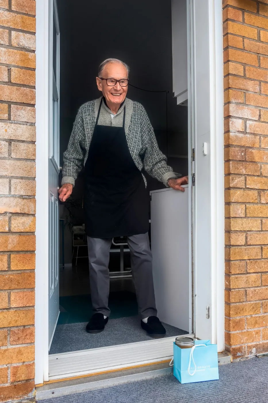 Un signore anziano apre sorridente la porta di casa