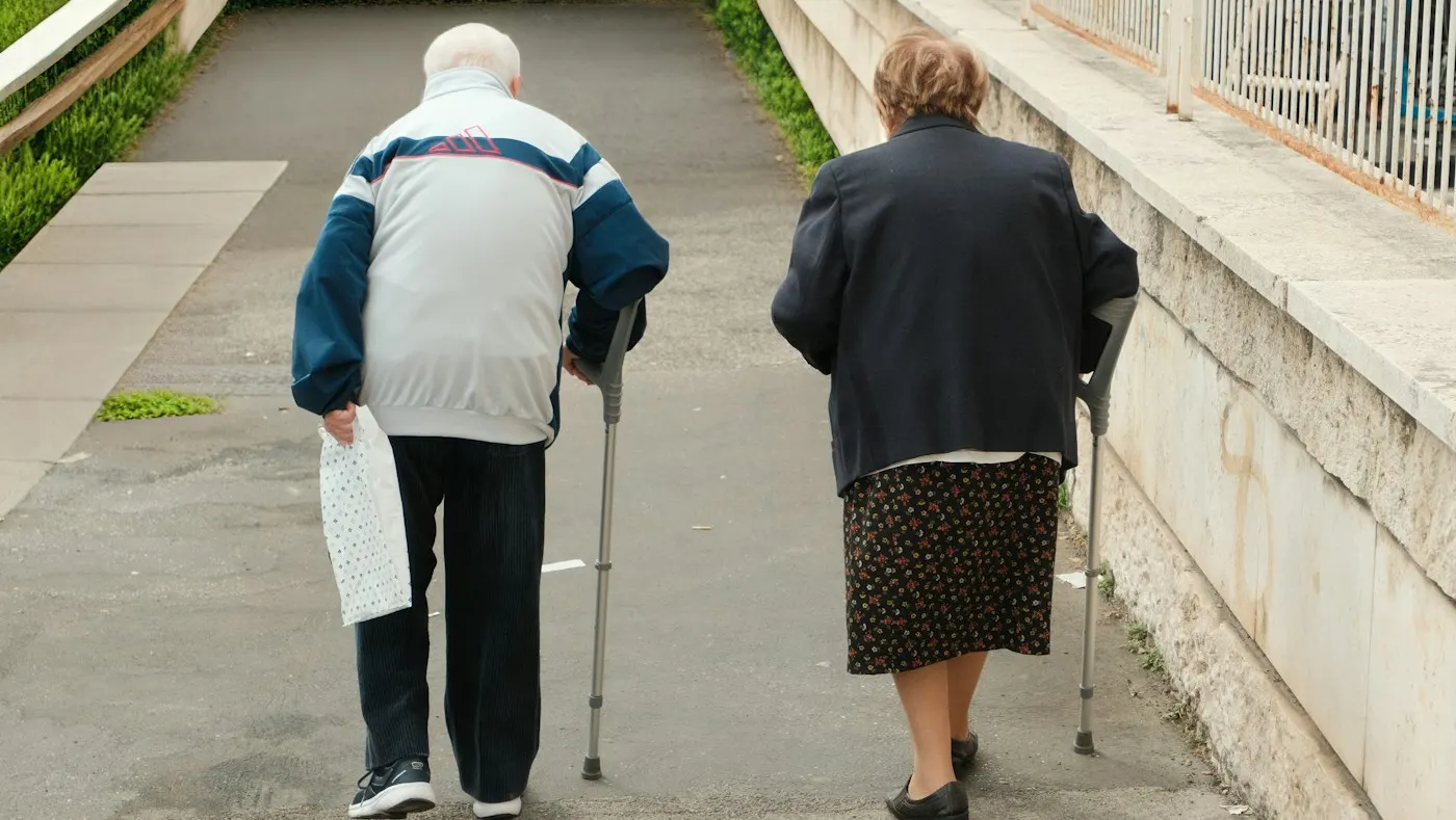 Due persone anziane camminano con il bastone lungo un vialetto